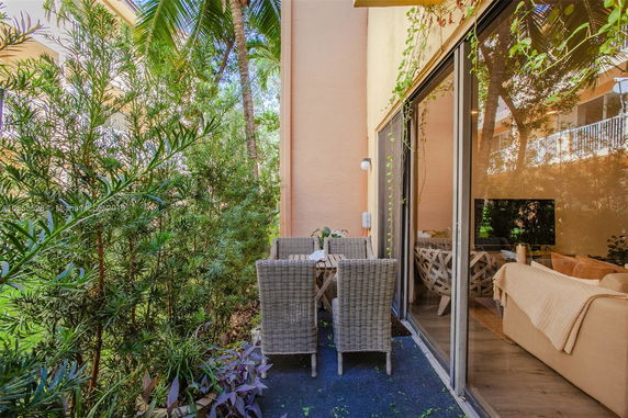 Outdoor patio area with a small table and chairs adjacent to a sliding glass door, surrounded by lush greenery.