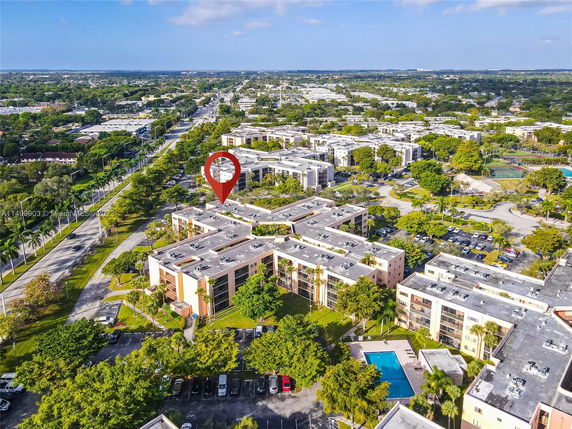 Aerial view of a multi-story residential complex with adjacent parking and surrounding greenery.