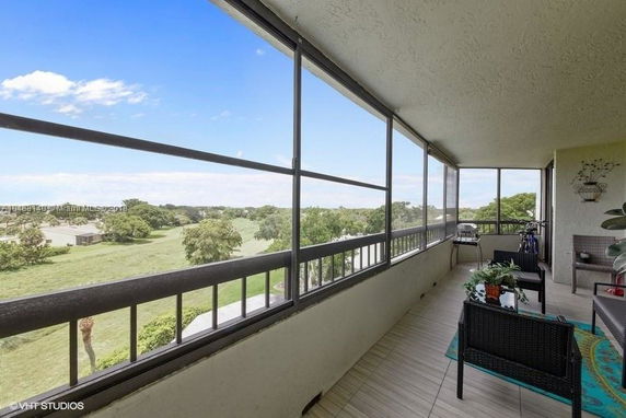 Balcony view from a building overlooking a grassy landscape with trees in the distance.