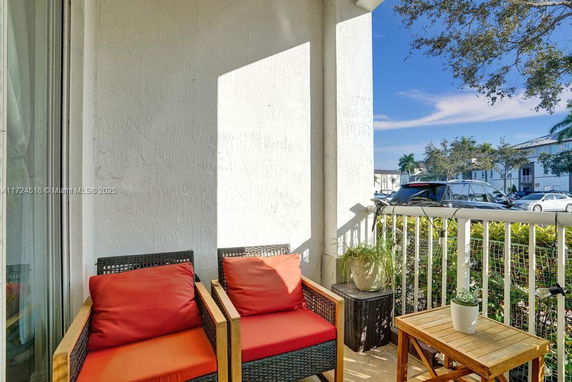 Outdoor patio with chairs and a small table, overlooking a residential parking area.
