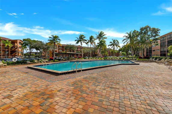 Outdoor swimming pool area with surrounding buildings and palm trees.