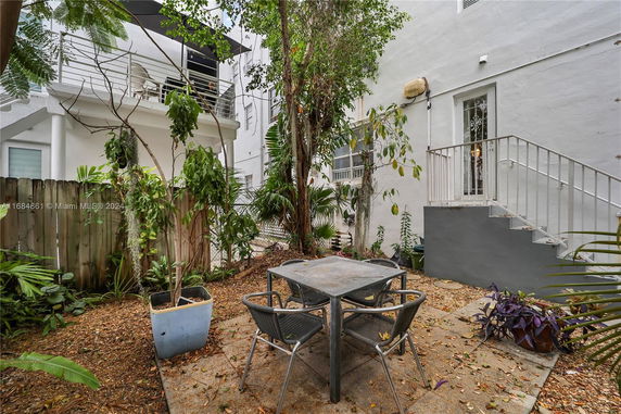 Outdoor area with a table and chairs surrounded by trees and adjacent buildings.