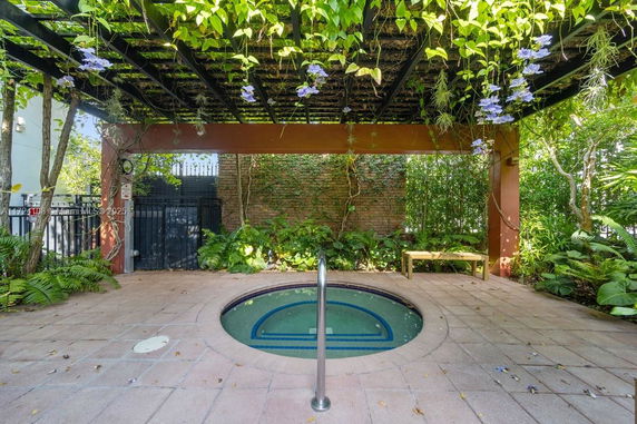 Outdoor area with a small round pool under a pergola with hanging plants.