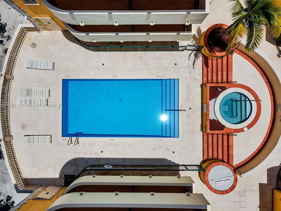 Top view of a swimming pool area with surrounding lounge chairs and adjacent hot tub.