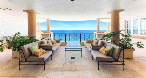 Covered outdoor seating area with a view of the ocean, featuring cushioned sofas and a glass-top table.