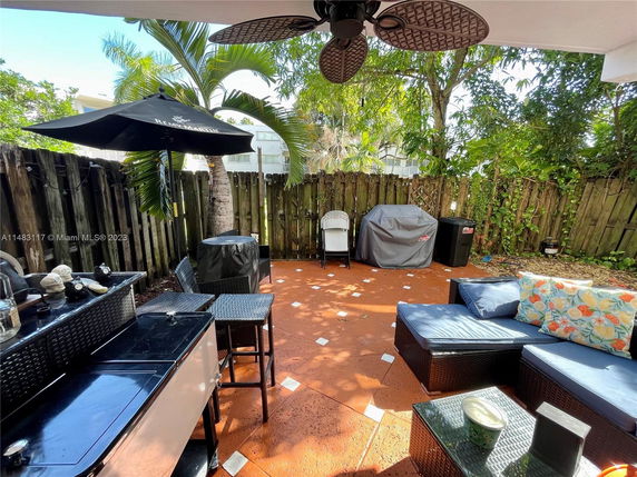 Outdoor patio area with seating, umbrella, and grill surrounded by a wooden fence and trees.