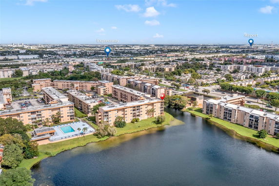 Panoramic view of a residential complex near a lake, with roads, trees, and cityscape in the background.