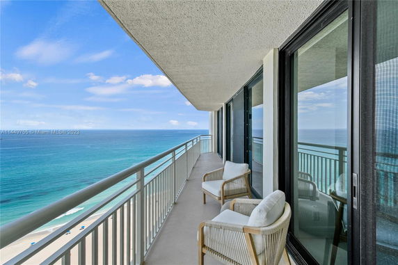 Balcony of a high-rise building overlooking the ocean with seating area.