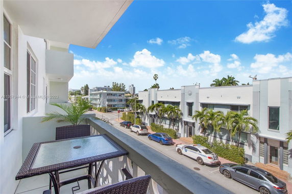View from a balcony overlooking a street with buildings and parked cars.