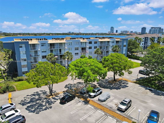 Front view of a multi-story residential building with balconies and a parking area in front.