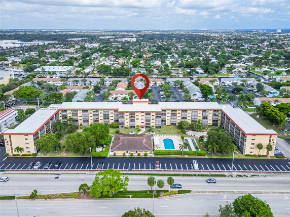 Aerial view of a multi-story building with a swimming pool, surrounded by a neighborhood and roads.