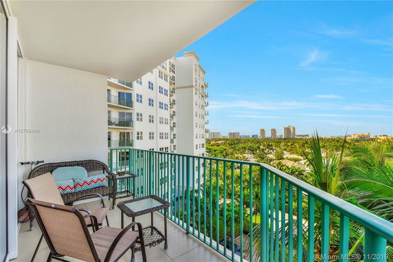 View from a balcony overlooking distant buildings and greenery, with nearby residential structures.