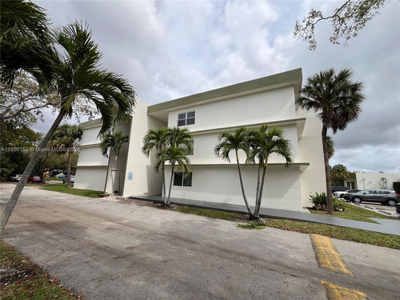 Front view of a modern multi-story building with a minimalist design and palm trees.