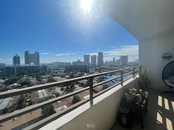 Panoramic view from the balcony showing a cityscape with tall buildings and a bright sun.