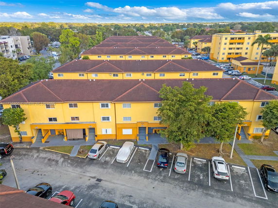Front view of a multi-story yellow apartment building with parking spaces.