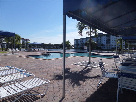 View of a swimming pool area with lounge chairs and nearby multi-story buildings in the background.