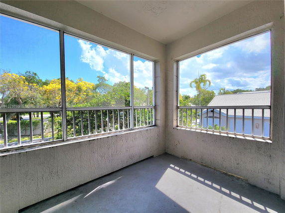 View from a balcony with railing and glass panels overlooking trees and a nearby building.