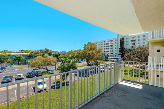 View from a balcony overlooking a parking area and residential buildings.