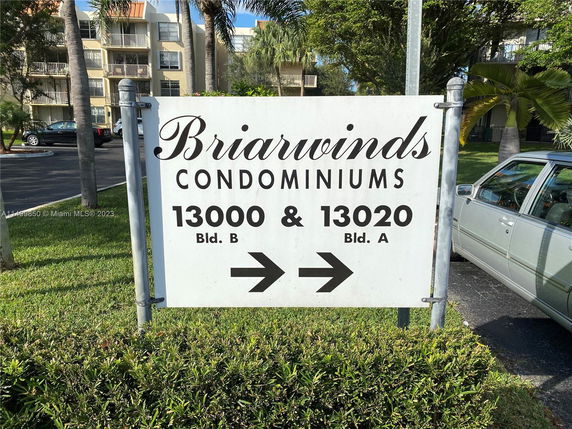 Sign for Briarwinds Condominiums with surrounding greenery and buildings in the background.
