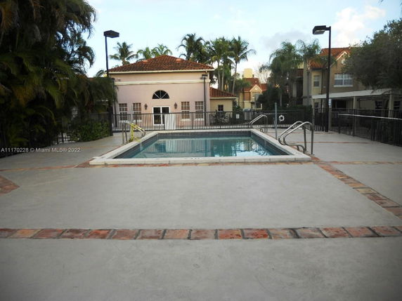 Outdoor swimming pool surrounded by a concrete deck and fenced area.