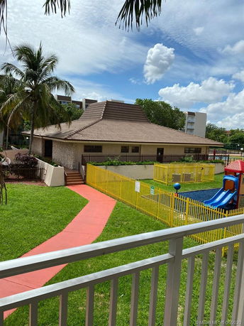 A building with a unique sloped roof, surrounded by a fenced playground and greenery.