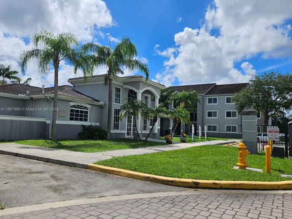 Front view of a two-story building with palm trees and a tiled roof.