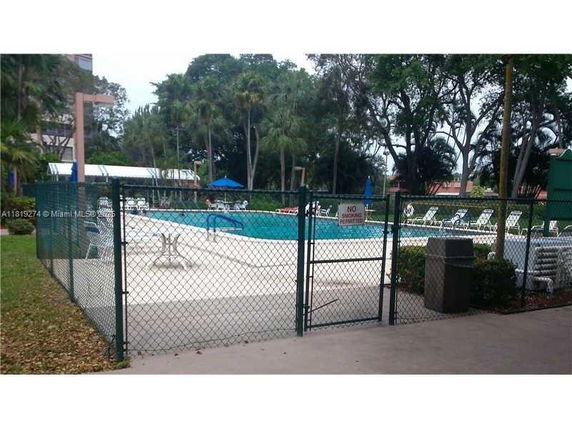 Outdoor swimming pool with surrounding fence and lounge chairs.