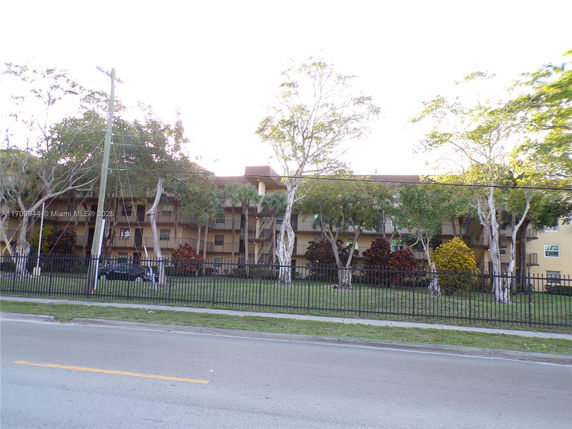 Front view of a multi-story residential building with balconies and trees in front.