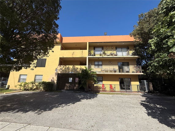 Front view of a multi-story yellow building with balconies and a gated entrance.