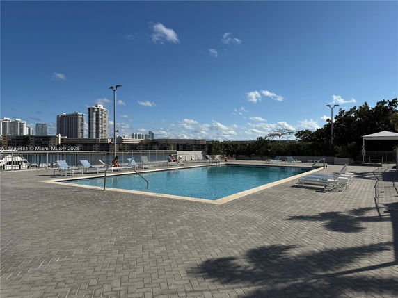 Outdoor swimming pool with lounge chairs, surrounded by buildings.