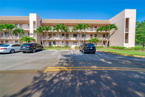 Front view of a three-story apartment building with balconies and parking spaces.