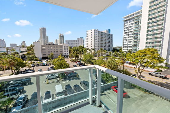 View from a balcony showing high-rise buildings and a parking area.