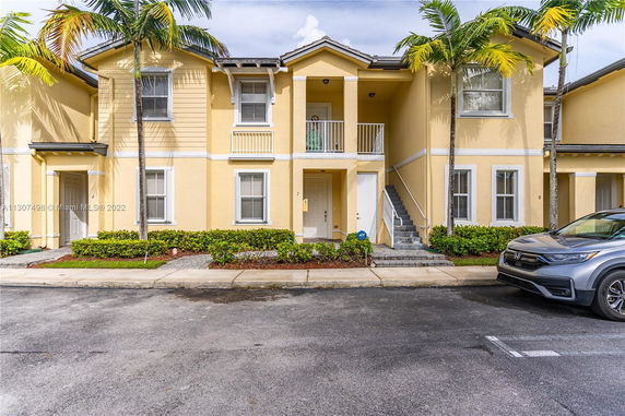 Front view of a two-story yellow house with a balcony and multiple windows.