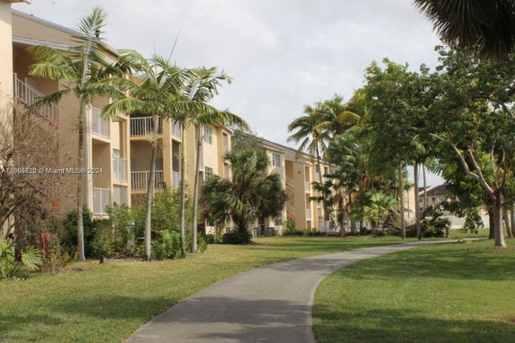 Exterior view of multi-story apartment buildings with balconies, surrounded by palm trees and a walkway.
