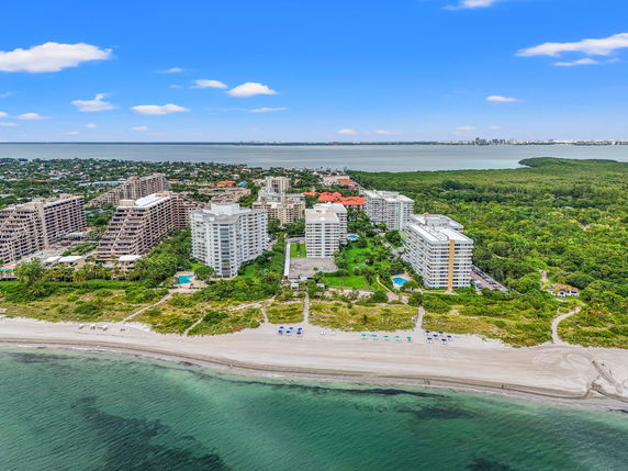 Aerial panoramic view of beachfront apartment buildings with surrounding greenery and ocean.