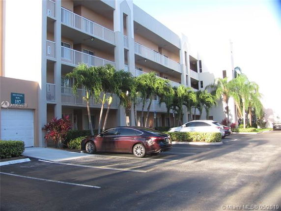 Front view of a multi-story building with balconies and adjacent parking area.