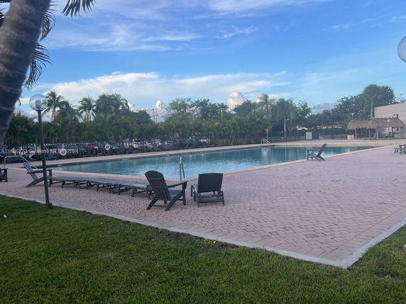 Outdoor swimming pool area with lounge chairs and trees in the background.