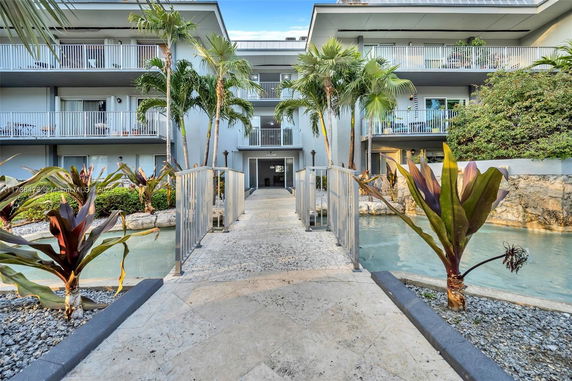 Front view of a multi-story building with balconies and a pathway over a small water feature.