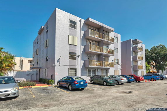 Four-story apartment building with balconies and adjacent parking area.