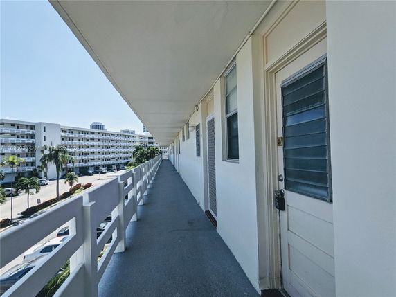 Exterior walkway of a multi-story residential building with other buildings and cars in the background.