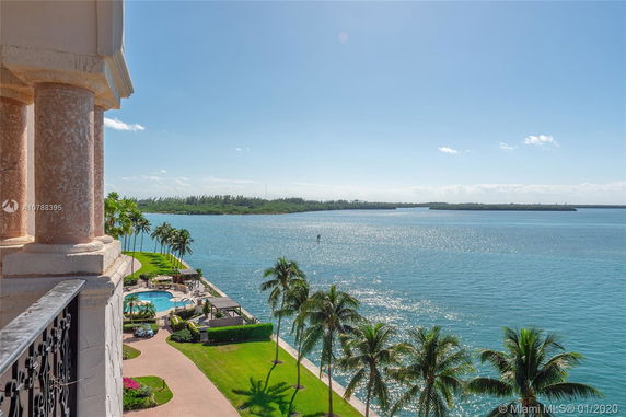Panoramic view from a building overlooking a waterfront area with palm trees and a pool.