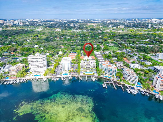 Aerial view of waterfront buildings with nearby docks and boats, surrounded by a lush green landscape.