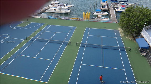 Two tennis courts adjacent to a waterfront with docks and boats.