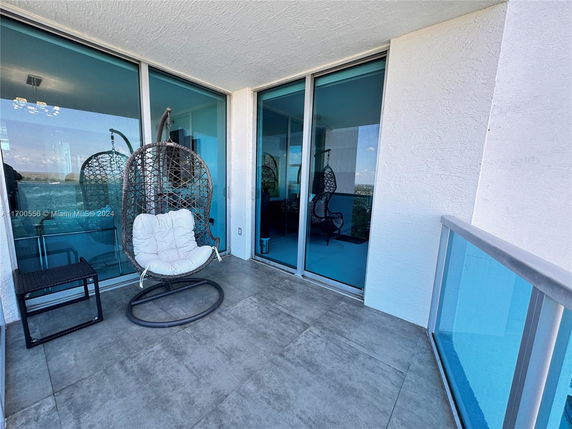 Balcony with a hanging chair and glass railing overlooking cityscape.