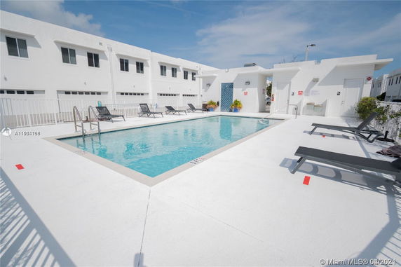 Outdoor swimming pool area with lounge chairs and white buildings in the background.