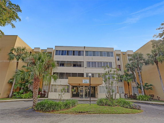 Front view of a multi-story apartment building with balconies and surrounding palm trees.