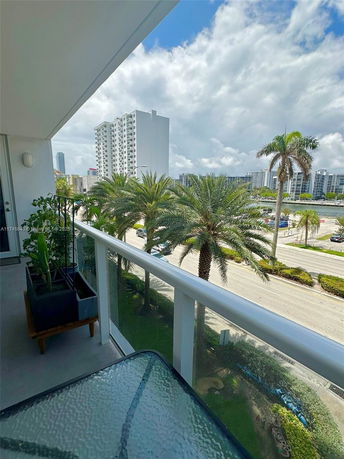 View from a balcony overlooking a road lined with palm trees and high-rise buildings.