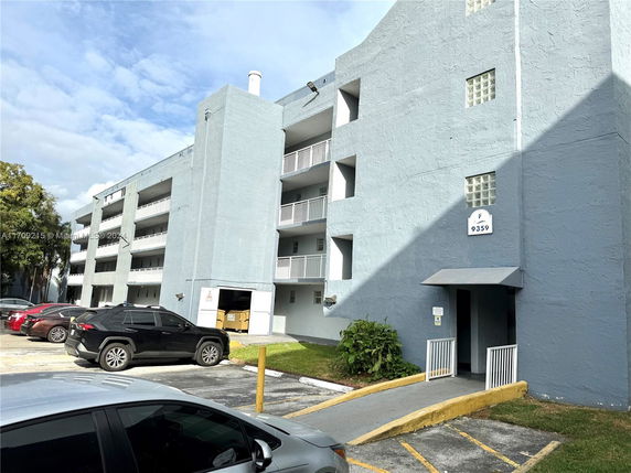 Front view of a multi-story building with balconies and parking area.