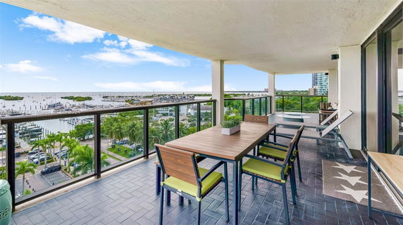 Balcony with outdoor furniture offering a wide view of a marina and surrounding greenery.