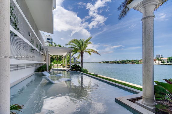 Outdoor area of a building with a water feature and lounge chairs overlooking a body of water.